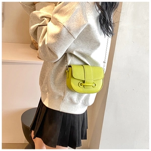 Détail d'un sac selle vert citron avec chaîne perlée, cuir texturé et boucle ronde