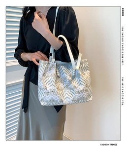 Detail of elegant wave pattern embroidery on tote bag with pearl handle and shoulder strap