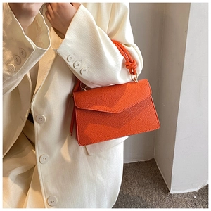 Close-up of orange textured leather handbag with a knotted handle and V-flap design