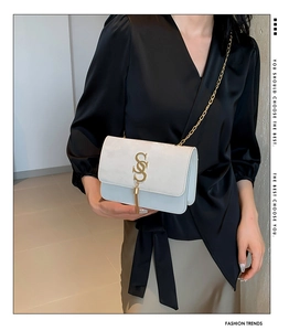 Detail of white PU leather crossbody bag with golden S logo and chain tassel fringe