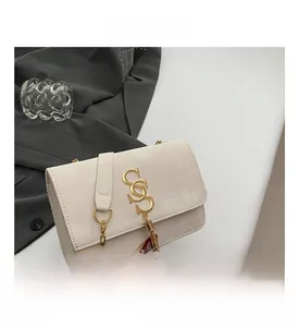 Detail of a creamy beige crossbody bag showing its gold S-shaped buckle and metal tassel