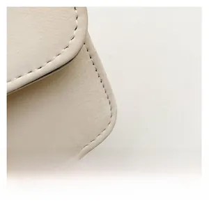 Macro detail of the creamy white leather texture and neat stitching of the shoulder bag