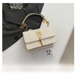 Macro detail of creamy white flap bag with golden tassel logo and smartphone for scale