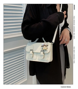 Close-up of beige satchel bag featuring dual silver buckles and a floral doll charm