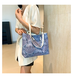 Detail of printed fabric tote bag with wave patterns, pearl chain, and leather handles