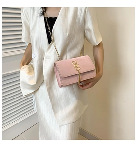 Pink velvet shoulder bag with gold chain and S-shaped tassel detail on white blazer