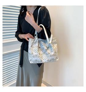 Close-up of elegant wave pattern embroidery and faux pearl accents on a bamboo-style tote bag