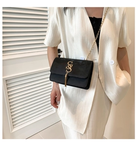 Detail of black crossbody bag with gold S-buckle and chain strap on a white suit