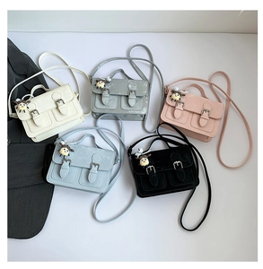 Flat lay of multiple colorful faux leather crossbody bags with cute doll charms and flap cover