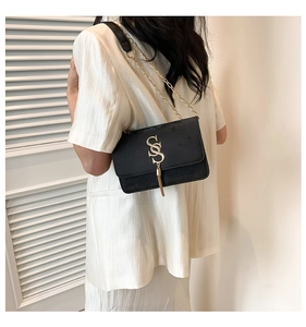 Chic black shoulder bag with gold S-buckle and tassel on a white suit model