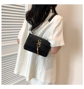 Detail of a black velvet shoulder bag with a gold tassel logo on a model in white