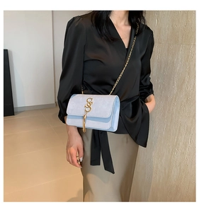 Close-up of light blue flap crossbody bag with gold chain strap and tassel detail