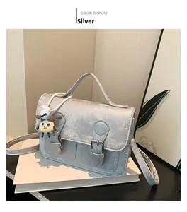 Detail of silver matte satchel bag showing buckled straps and cute doll pendant