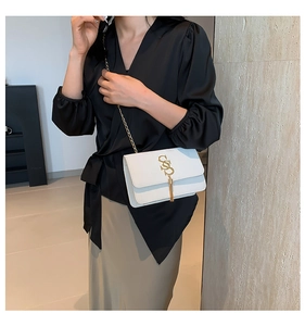 Close-up of white leather shoulder bag featuring a gold S-shaped buckle and fringe detail