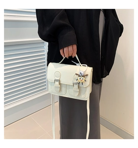 Detail of cream satchel bag with dual buckles, top handle and cute cartoon charm