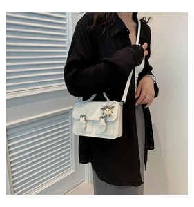 Detail of a beige vintage square bag with buckle straps and a cute cartoon charm