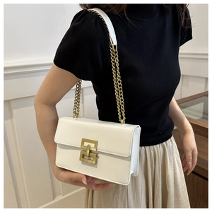 Close-up of a white leather crossbody bag with a gold geometric lock and chain strap