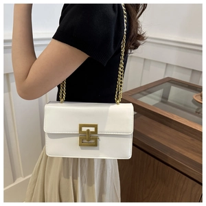 Detail of white chain crossbody bag featuring a golden geometric clasp and luxury texture