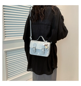 Detailed view of a light blue metallic crossbody bag with a cute charm on a model