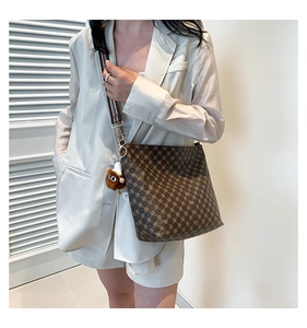 Detail of a brown geometric print tote bag with striped strap and a plush owl charm