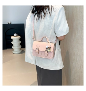 Pink Cambridge style crossbody bag with cartoon pendant shown on model in modern room