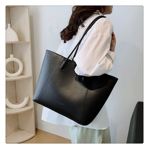 Gros plan du sac cabas noir en cuir grainé porté par un mannequin dans une chambre