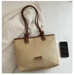 Detail of herringbone weave straw tote with brown leather strap and phone for scale