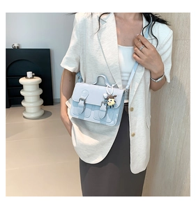 Detail view of light blue satchel bag with metallic buckles and cute cartoon charm