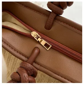 Detail of smooth metal zipper and premium brown lychee leather on a woven tote bag