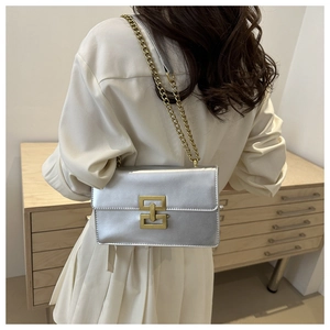 Detail of silver crossbody bag with golden geometric clasp and metal chain strap on model