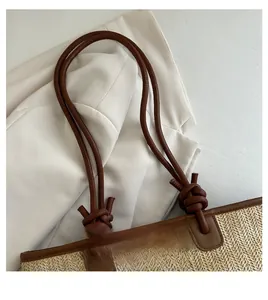 Detail of woven straw bag with dark brown leather handles and decorative knots