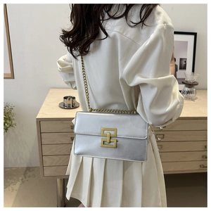 Sac à bandoulière argenté avec fermoir bronze porté par un mannequin dans un décor minimaliste