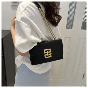 Detail of elegant black chain crossbody bag featuring a large gold geometric buckle