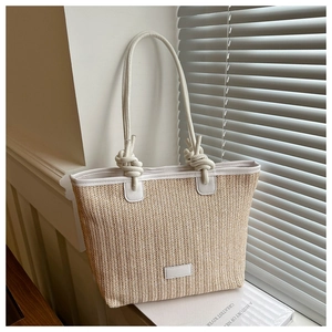Detailed view of woven straw tote bag with white leather straps and knot accents