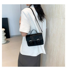 Detailed view of a vintage black leather satchel worn over the shoulder by a model