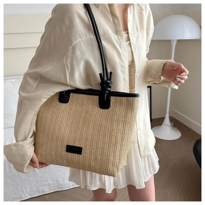 Detail of woven straw tote with black leather trim and knot handle on a model
