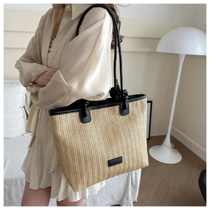 Detail of herringbone woven straw tote bag with black leather shoulder straps and knotted accents