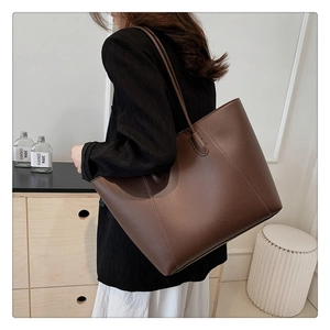 Détail de la texture en cuir litchi marron foncé sur un grand sac cabas fourre-tout
