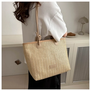 Detail of woven straw tote bag featuring brown leather trim and knotted shoulder strap