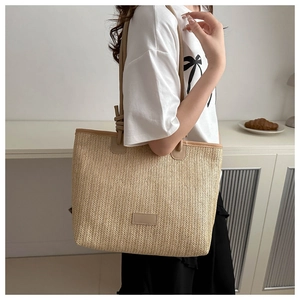 Close-up of woven straw tote bag with brown leather handles and a minimalist logo patch