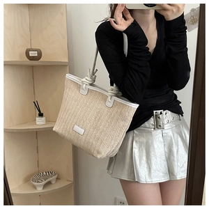 Detail of woven straw tote bag with white V-pattern and decorative rope knot handles
