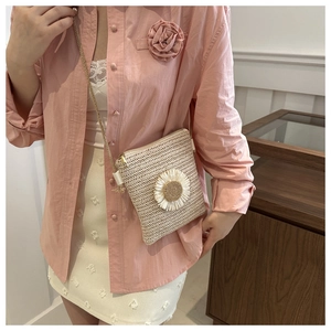 Detail of straw woven square bag with white daisy decoration and thin shoulder strap
