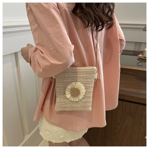 Detail of straw woven crossbody bag with white daisy decoration on beige material