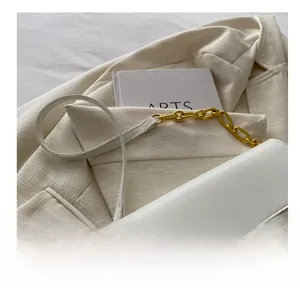 Detail of white leather shoulder strap with golden metal chain links on tweed fabric