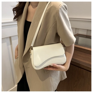 Close-up of cream white shoulder bag with unique asymmetrical flap on beige suit
