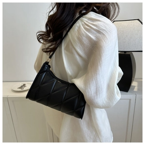 Detail of black quilted shoulder bag with gold zipper worn by a model in a modern room