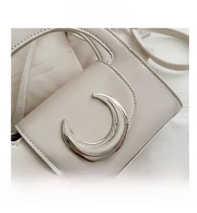 Close-up of a smooth beige leather shoulder bag featuring a polished silver crescent buckle
