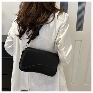 Detail of a minimalist black crossbody bag featuring a unique wavy flap design and slim strap