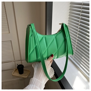 Detail of bright green quilted baguette shoulder bag held in natural window sunlight