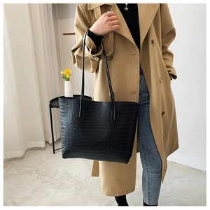 Detail of black crocodile embossed tote bag paired with a trench coat for urban style